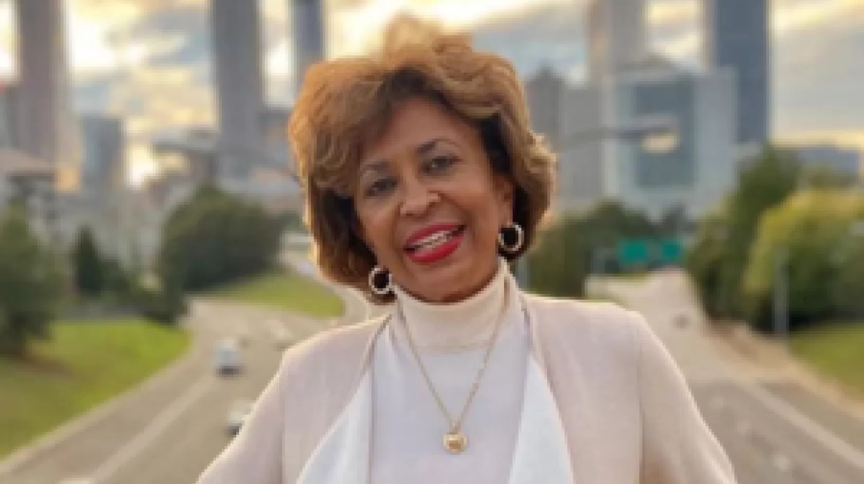 A woman poses on a bridge with a city in the background