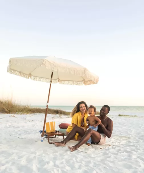 A family poses on the beach at sunset under a beach umbrella